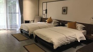 Une chambre d’hôtel avec deux lits, une chaise, un bureau et une grande fenêtre avec des rideaux légers.