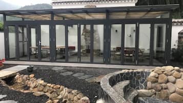 A modern building with a glass facade, outdoor seating area, and a stone water feature.