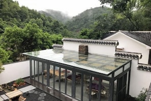 A modern glass-roofed room with a view of a lush forested hillside. - Yunjishan Hotspring Holiday Village (Xinfeng)