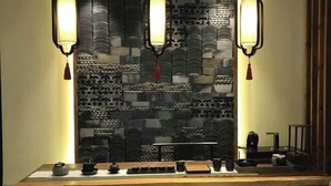 Une pièce avec une longue table en bois, des théières noires, des tasses et un service à thé. Trois lampes murales, ornées de glands, y sont fixées.