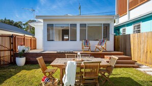 Une maison blanche avec une terrasse, des meubles en bois et une chaise colorée.