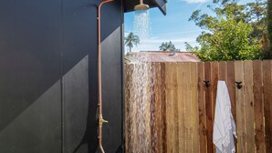 Un tuyau métallique menant à un pommeau de douche, avec de l’eau qui s’écoule sur une clôture en bois.