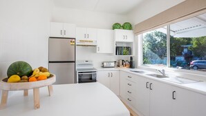 Une cuisine moderne avec des armoires blanches, un réfrigérateur en acier inoxydable, un four, un four à micro-ondes et une grande fenêtre donnant sur l’extérieur.