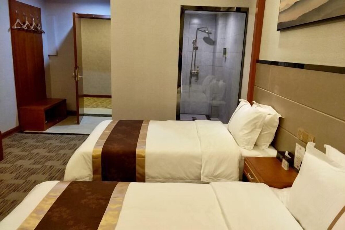 A hotel room with a bed, a nightstand, a wooden bench, a shower area, and a coat rack.