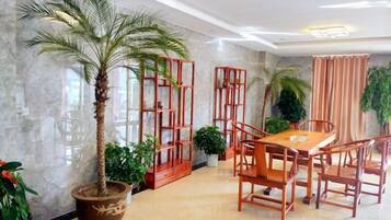 Un espace repas avec un mur en marbre, une table en bois et des chaises. On y trouve également des plantes en pot et un grand arbre en pot.
