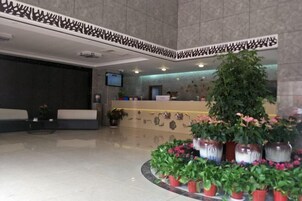 Un vestíbulo con mostrador de recepción, zona de estar y plantas decorativas.