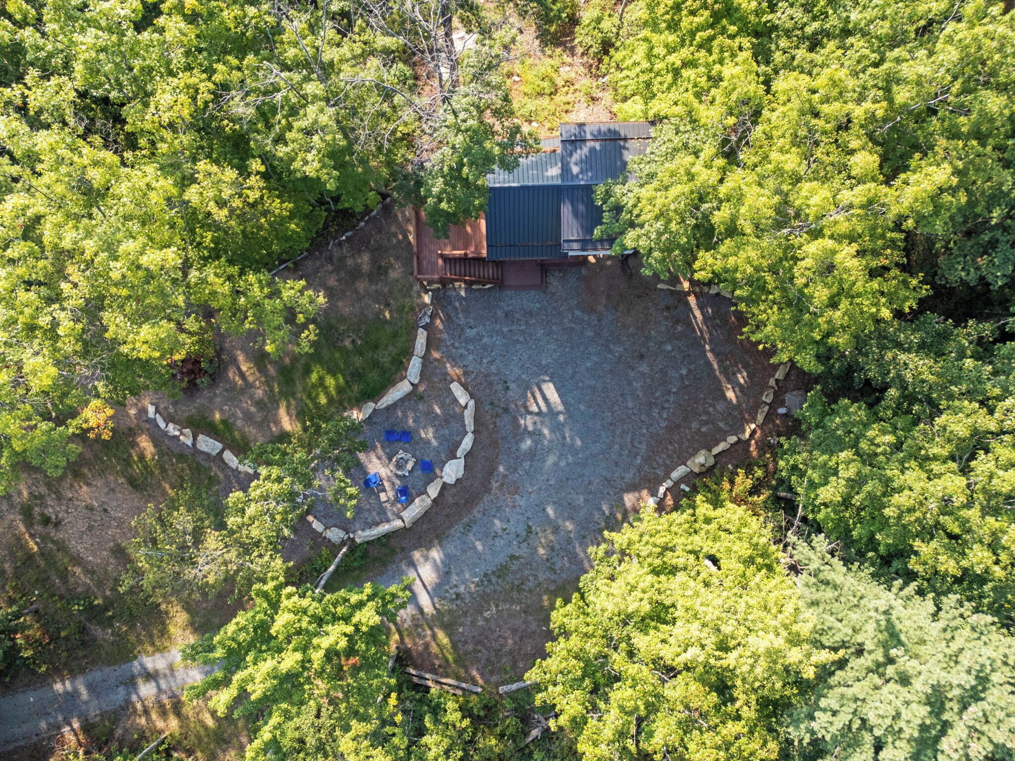 An aerial view of a property surrounded by dense trees, featuring a fenced area with a stone pathway and a small wooden structure.