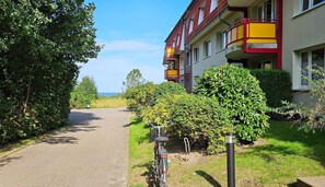 Polku johtaa rakennukseen, jonka julkisivu on punainen ja keltainen. Rakennuksen ympärillä on vehreää kasvillisuutta ja taivaalla ei ole pilviä.