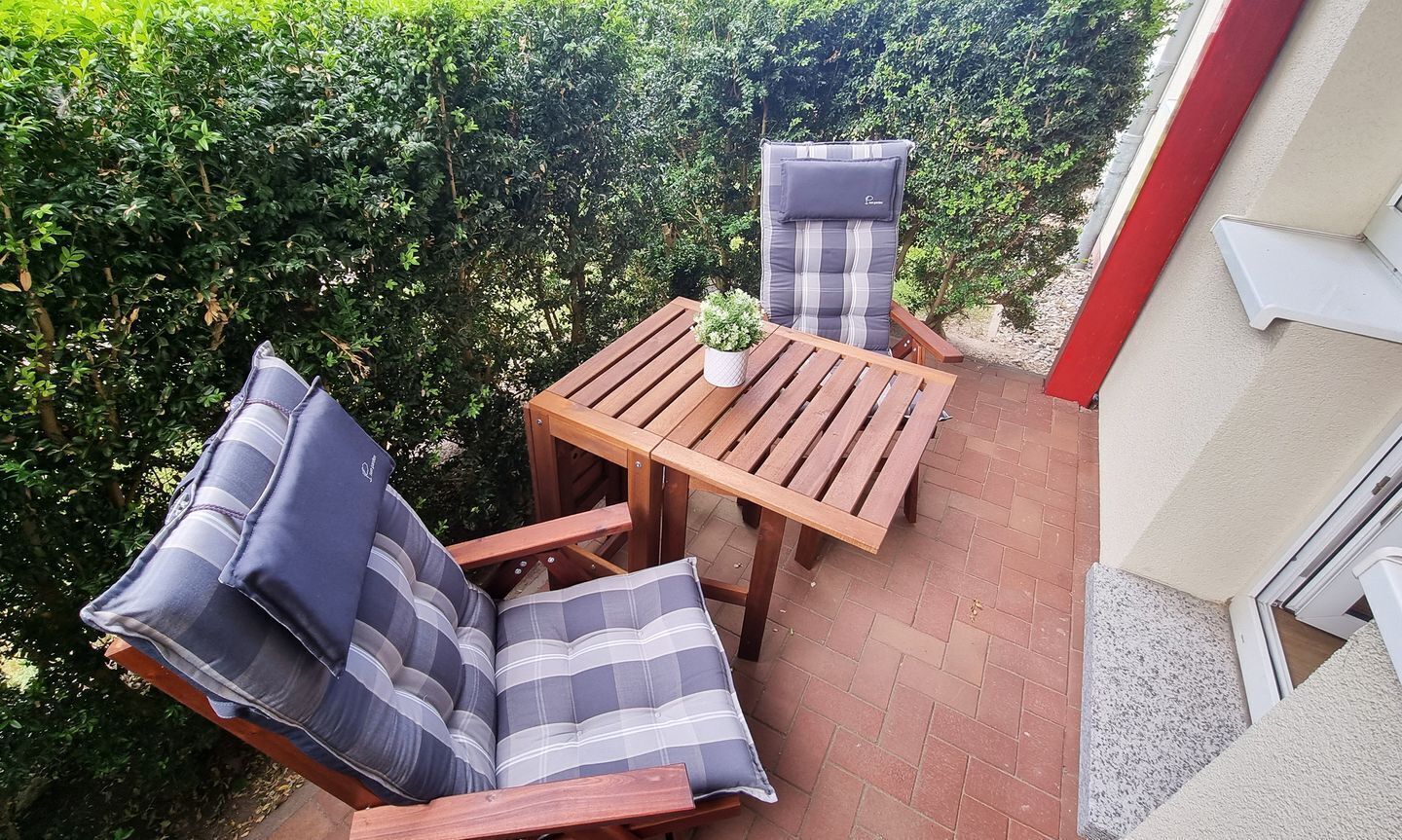 A patio with a wooden table and two striped cushioned chairs.