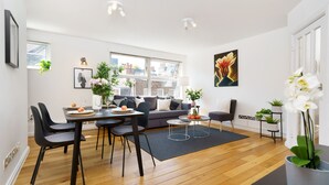 Een moderne woonkamer met een eethoek, met een bank, stoelen, een salontafel en een groot raam met uitzicht op de stad.