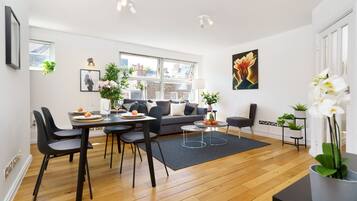 Un salon moderne avec un coin repas, comprenant un canapé, des fauteuils, une table basse et une grande fenêtre donnant sur la ville.