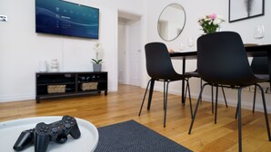 Een moderne woonkamer met een flatscreen-tv, zwarte stoelen, een eettafel en een salontafel met een gamecontroller.