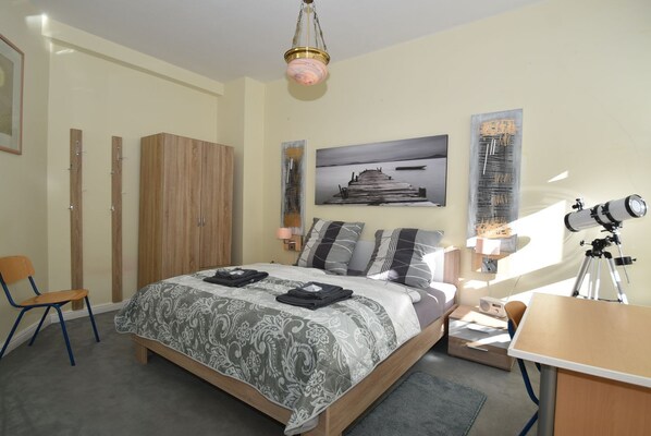 A bedroom with a bed, a desk, a chair, a wardrobe, and a telescope.