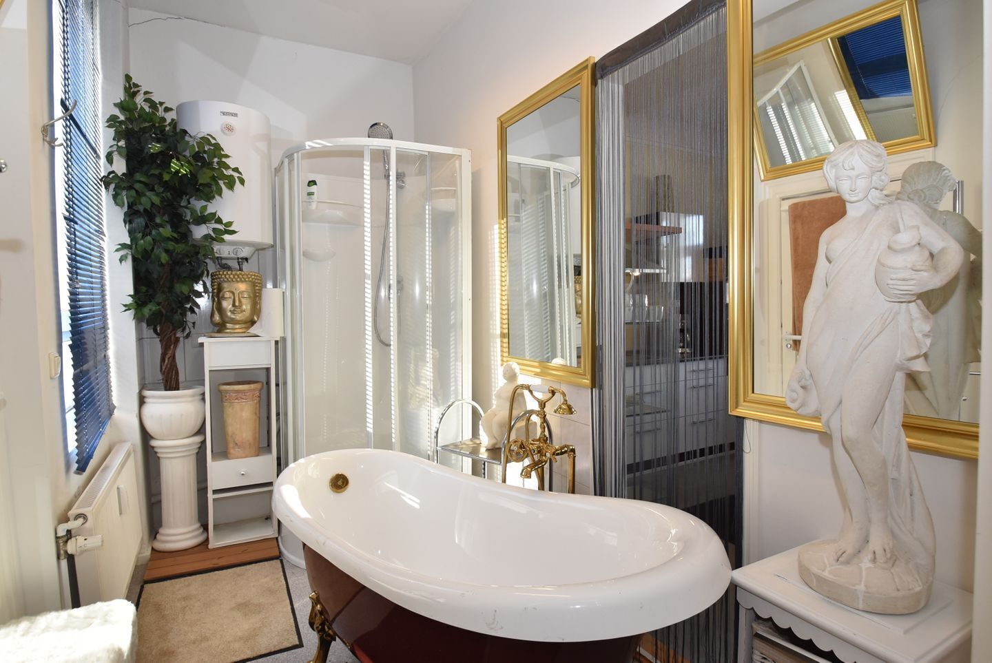 A bathroom with a freestanding bathtub, a shower enclosure, a large mirror, and a statue.