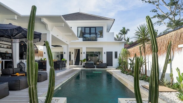 Een modern huis met een zwembad, omgeven door cactussen en palmbomen.