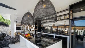Een moderne keuken met een zwart marmeren eiland, zwarte rieten hanglampen en een stenen wand.