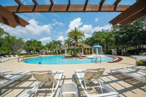 Relax by the resort pool surrounded by lounge chairs and a palm tree, under a shaded pergola.