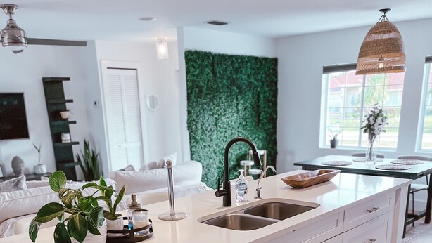 Una cocina moderna con una isla grande, armarios blancos y un detalle de pared verde.