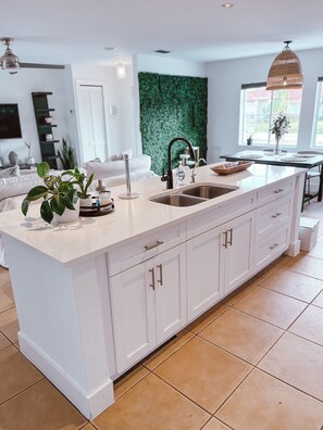 A modern kitchen with a large island, white cabinetry, and a green wall accent.