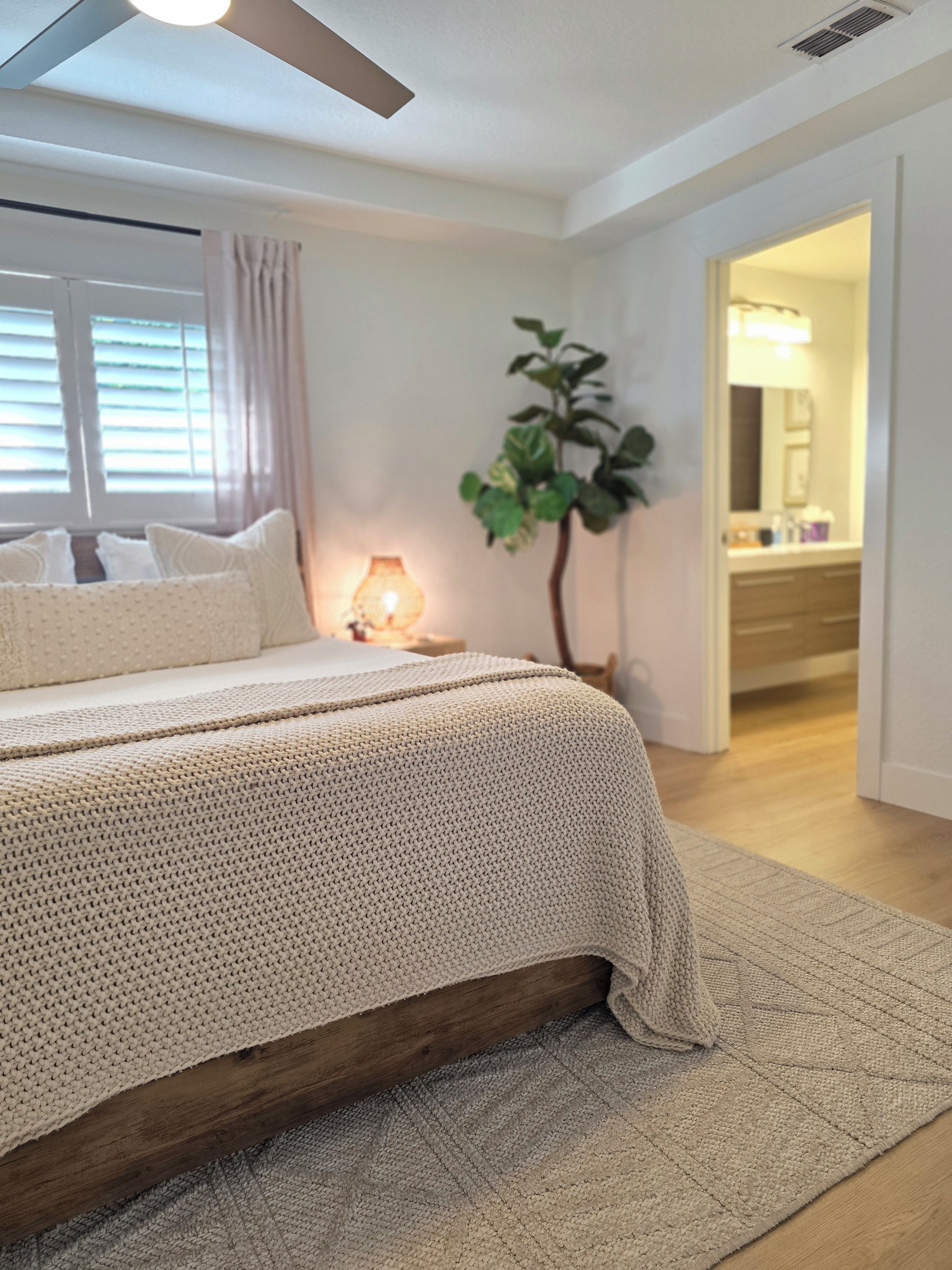 A bedroom with a bed, a bedside lamp, a plant, and a view of a bathroom.