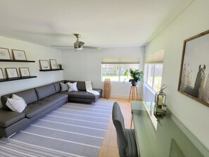 A modern living room with a sectional sofa, a glass coffee table, and a ceiling fan.