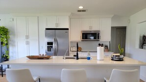 Una cocina moderna con armarios blancos, un refrigerador de acero inoxidable, un microondas y una isla grande con taburetes de bar.