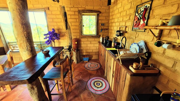 Una cocina rústica con una mesa de madera, sillas, una ventana y un muro de ladrillo.