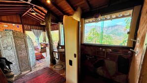 A rustic interior with a large window offering a mountain view, a wooden ceiling, and a cozy seating area with a patterned rug. - Ecopousada Toca do Guará (Alto Paraíso de Goiás)