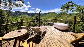 Una terraza de madera con sillones de descanso y un jacuzzi con vistas a un paisaje montañoso.