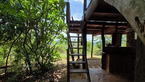A wooden staircase leading to a covered outdoor area with a view of a lush garden and a stone wall. - Ecopousada Toca do Guará (Alto Paraíso de Goiás)