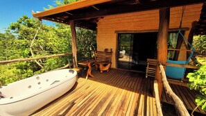 Una terraza de madera con un jacuzzi, sillas de madera y un ventanal que da a un área cubierta.