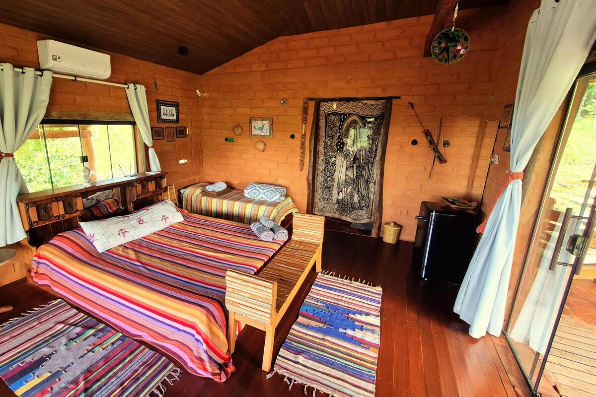 Um quarto acolhedor e rústico, com uma cama de madeira, uma pequena mesa de estudo e uma janela com cortinas.