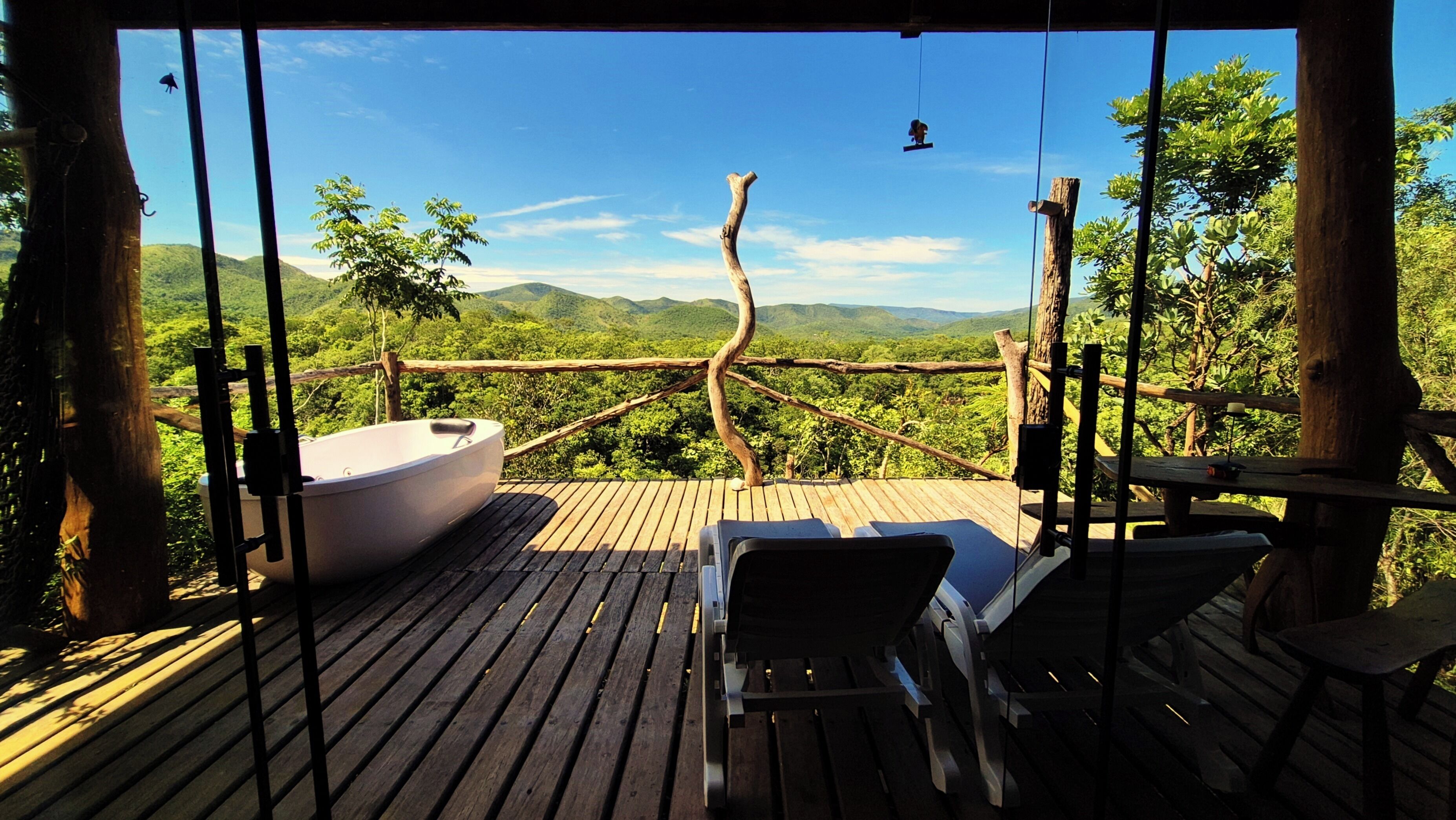 A wooden deck with a hot tub, lounge chairs, and a view of a mountainous landscape.