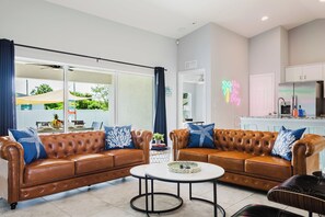 Een moderne woonkamer met leren banken, een salontafel, en een keukenhoek met kasten en een koelkast.