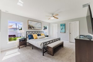 A bedroom with a bed, bedside tables, a bench, a ceiling fan, and artwork on the walls.
