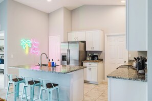 A modern kitchen with a central island, bar stools, a neon sign, and white cabinetry. - Relaxing Hot Tub Home, 2 King Beds, Dog-Friendly, Golf Course (Cape Coral)