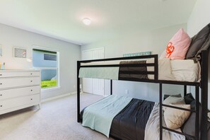 A bunk bed room with a dresser, a window with a view of grass, and a ceiling light.
