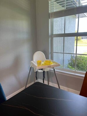 Un coin de pièce avec une chaise haute près d’une fenêtre, un plancher sombre et une vue partielle sur une autre chaise.