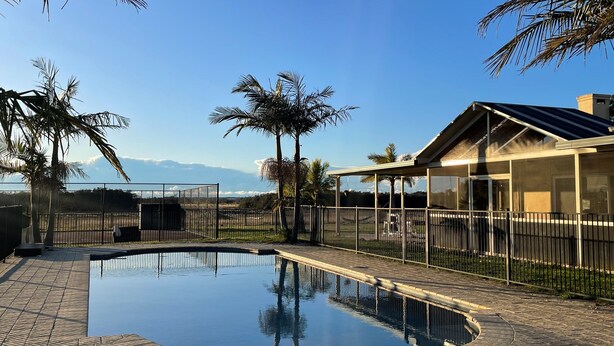 A swimming pool with a tiled deck, surrounded by a fence and palm trees. - Beautiful Large Country Home in the Perfect Location with tennis court & theatre (Worrigee)