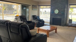 A spacious living room with a black leather sofa, a wooden coffee table, and a stone fireplace. - Beautiful Large Country Home in the Perfect Location with tennis court & theatre (Worrigee)