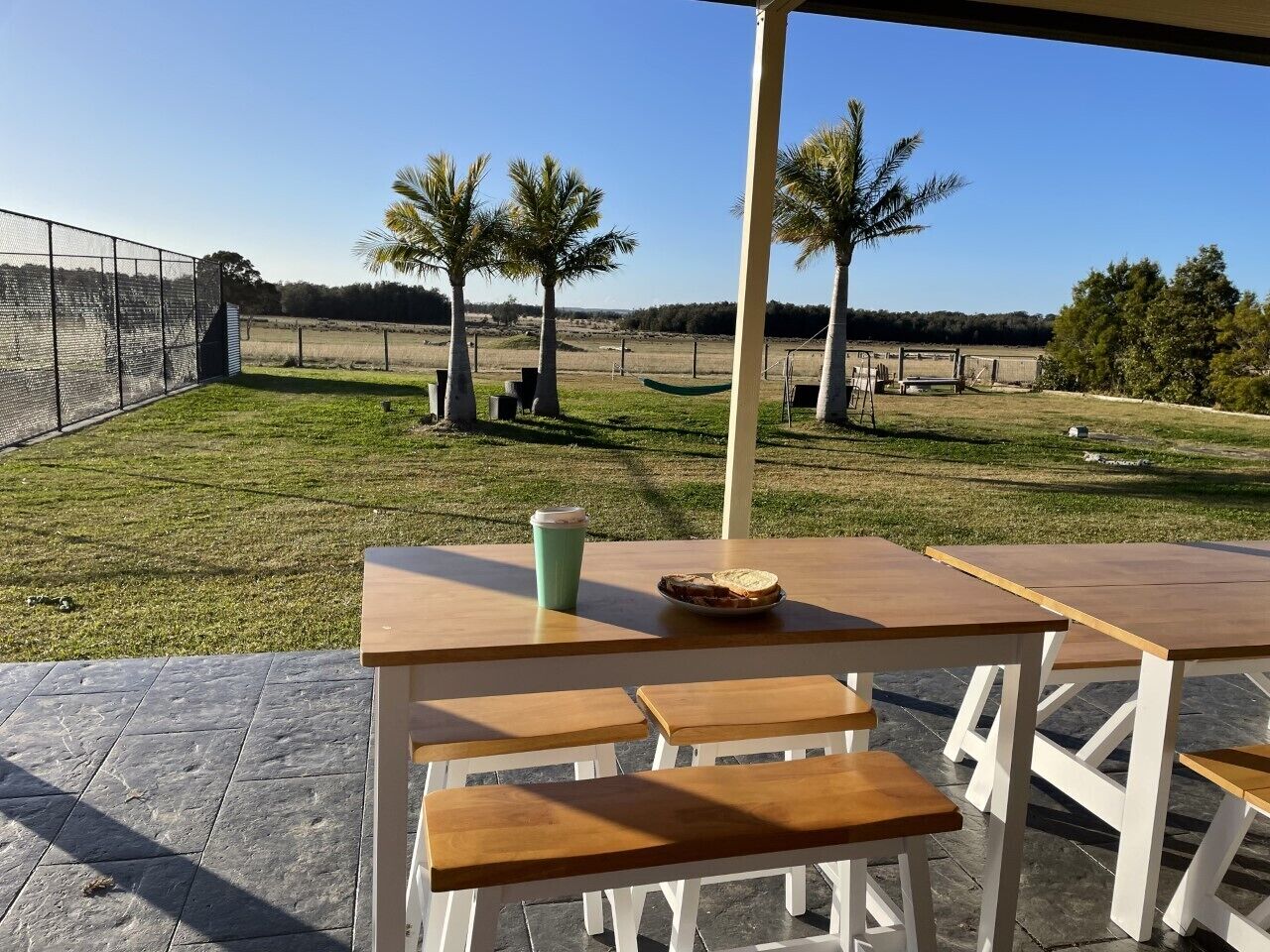 En udendørs patio med et bord og bænke, en kaffekop og et fad med mad.