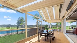 A covered patio with a glass balustrade overlooking a pool and lawn. - Beautiful Large Country Home in the Perfect Location with tennis court & theatre (Worrigee)