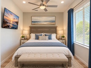 A bedroom with a bed, a ceiling fan, a large window with blinds, and two bedside tables with lamps.