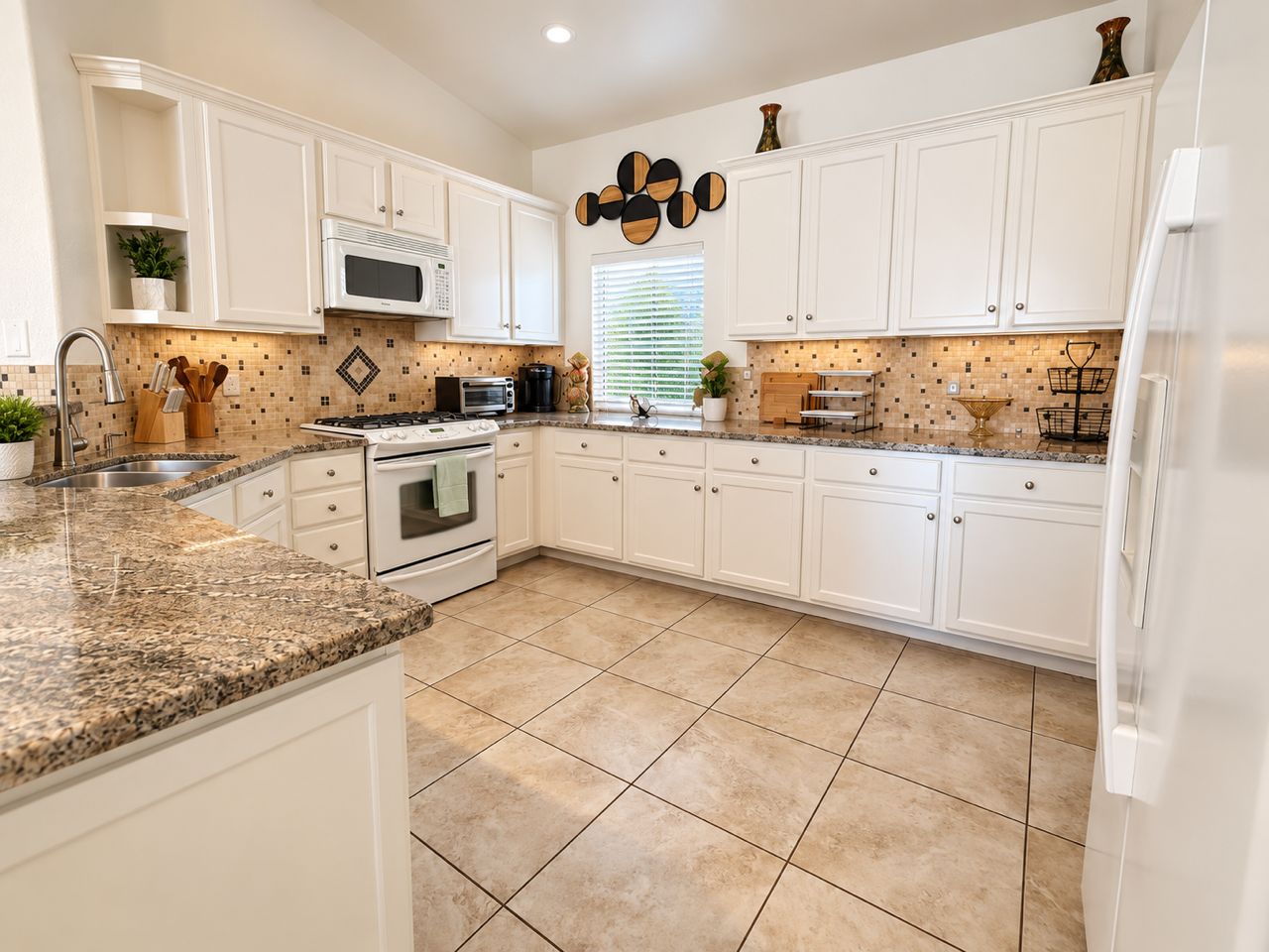 A kitchen with white cabinets, a granite countertop, a microwave, stove, and a refrigerator.