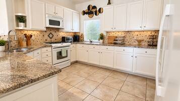 A kitchen with white cabinets, a granite countertop, a microwave, stove, and a refrigerator.