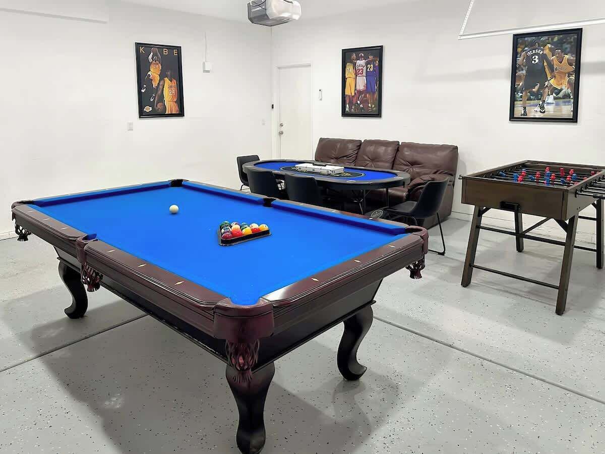 A pool table with balls, a foosball table, and two framed sports posters on the wall.