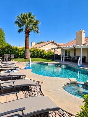 A swimming pool with lounge chairs, a palm tree, and a covered patio area.