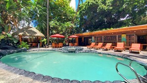 A pool area with lounge chairs and umbrellas, surrounded by tropical vegetation and a thatched-roof structure. - 7th floor Dreamy King bed Studio plus Futon and all modern touches (Honolulu)