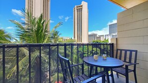 A balcony with a round table and chairs, overlooking a cityscape with tall buildings and palm trees. - 7th floor Dreamy King bed Studio plus Futon and all modern touches (Honolulu)