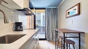 A compact kitchen with a built-in oven, a coffee maker, and a window with curtains. - 7th floor Dreamy King bed Studio plus Futon and all modern touches (Honolulu)